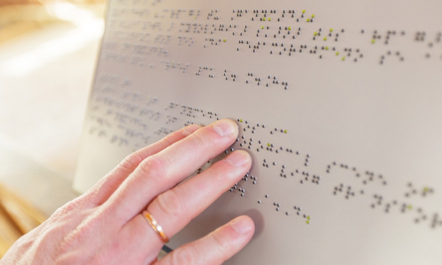 A hand reads Braille lettering.